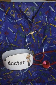 Photo of a medical scrub shirt, a stethoscope and a paper hat labeled "doctor"