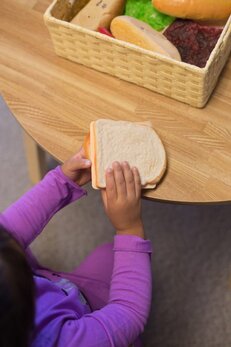 Photo of a young girls holding a pretend sandwich. In the background is a wicker basket holding pretend food.
