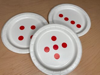 Photo of paper plates with dots arranged to show 4 (2 groups of 2 and a line of 4) and 5.