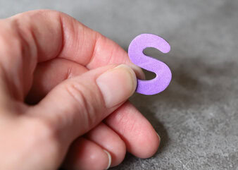 Photo of a hand holding a foam letter s magnet.
