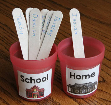 Photo of two red cups, labeled "Home" and "School." Student name sticks are placed in the cups to indicate attendance.