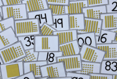 Photo shows cards with yellow place value blocks and numerals; demonstrating the game Place Value War.