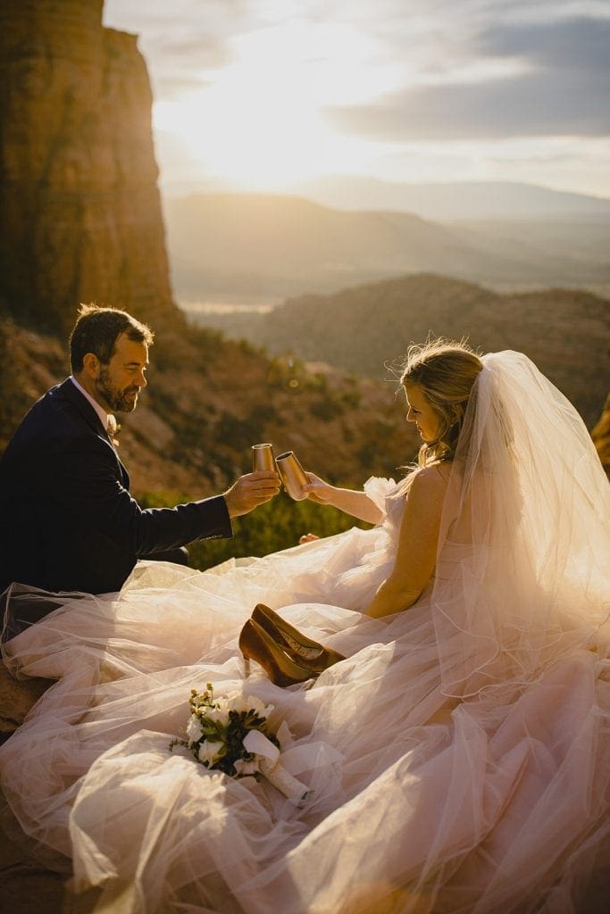 Bride and groom cheers their champagne glasses while watching the Sedona sunset