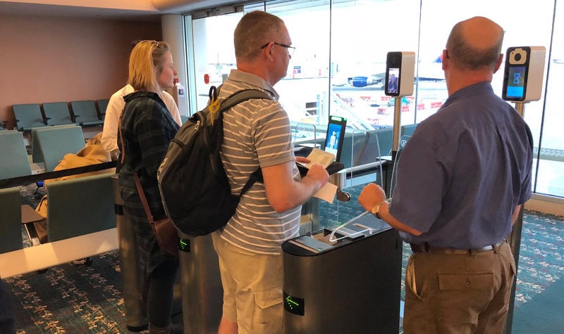 Travelers going through a facial recognition scanner.