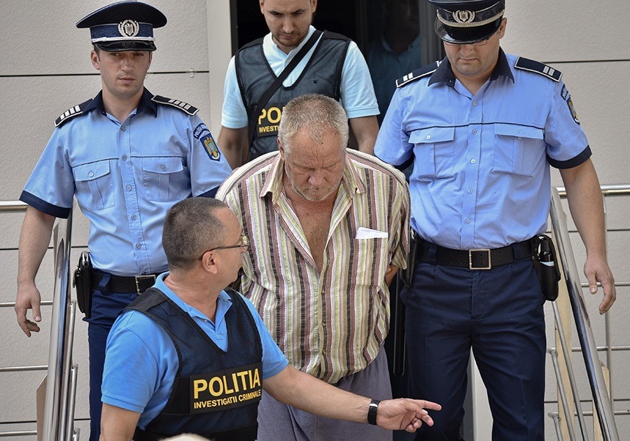 Police officers escort Gheorghe Dinca, the suspect in the case of rape and murder of a 15 year-old girl, from a court in Craiova, southern Romania, Saturday, July 27, 2019. Thousands of people took part Saturday evening in Bucharest in a march protesting the handling of the case, blaming Romanian officials for negligence, incompetence and a lack of empathy. (AP Photo/Bogdan Danescu)