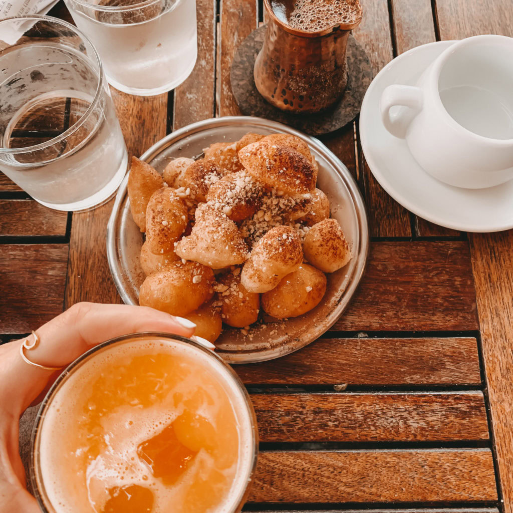 Loukoumades, frisch gepresster Orangensaft, Wassergläser und ein griechischer Macke im Kännchen