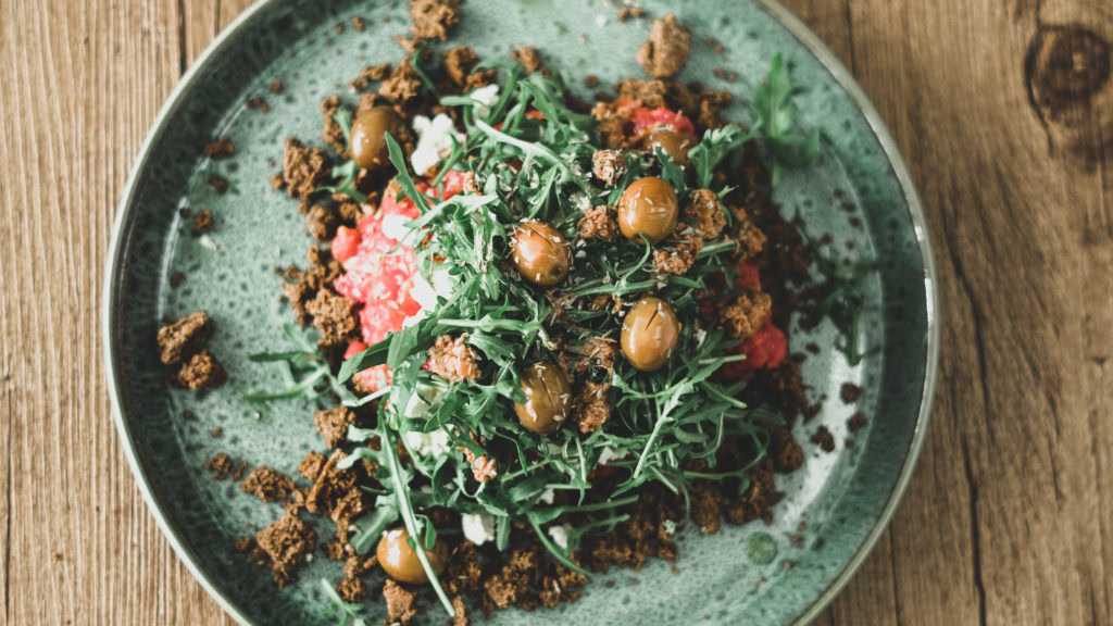 Dakos Salat mit Rucola und Oliven auf einem türkisen Teller