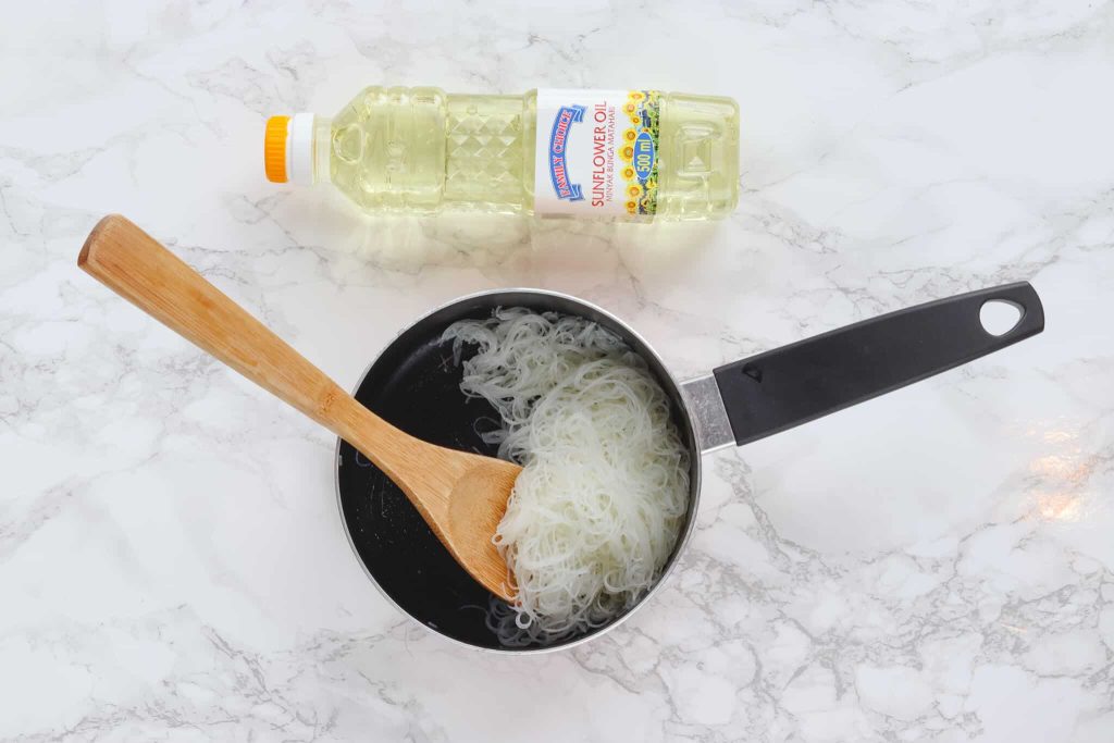 Rice noodles being tossed in oil in a saucepan