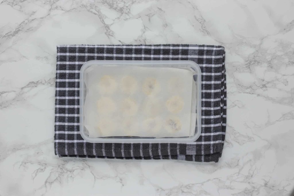 Banana slices in a Tupperware container covered with parchment paper