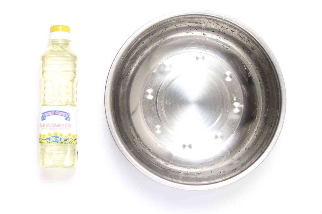 A bottle of sunflower oil next to a large metal bowl covered in oil without popcorn kernels.