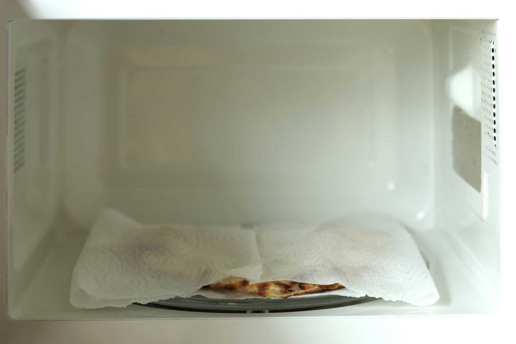 A piece of naan bread covered in a wet paper towel in the microwave