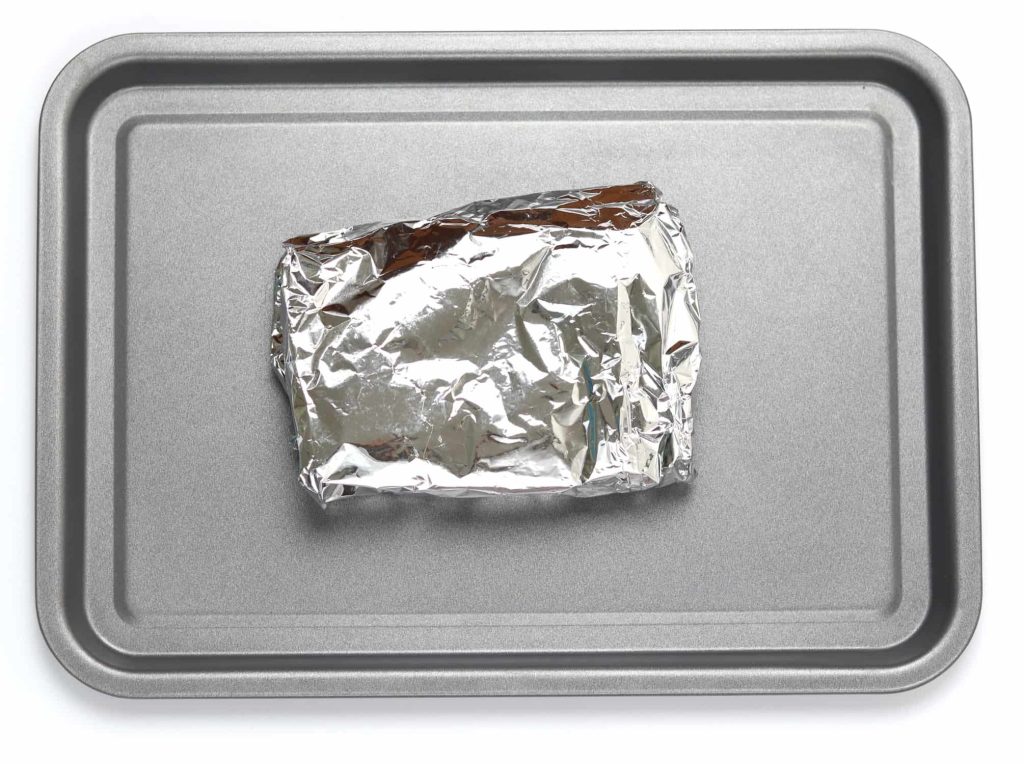 Piece of naan bread wrapped up in a foil parcel on a baking tray