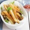 Homemade French Fries sit in a white ceramic bowl on a white wood tabletop with a glass bowl of ketchup, a salt shaker and a blue tea towel in the background.