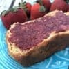 homemade strawberry jam on bread, on a teal plate, with strawberries on the plate