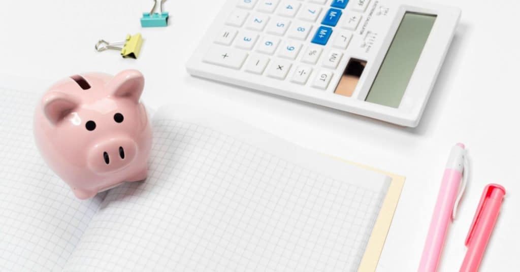 Pink piggy bank and calculator on desktop with open journal - how to track your spending