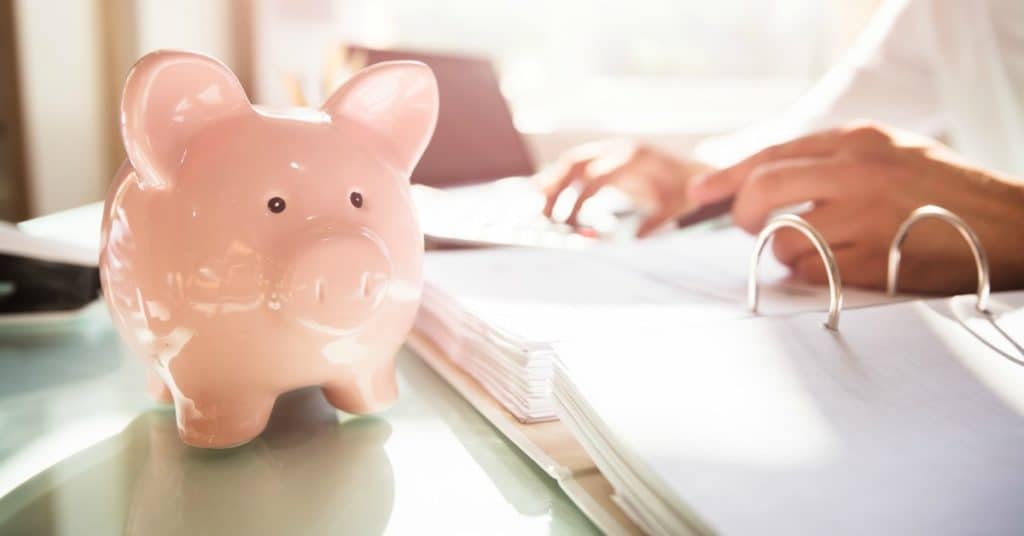 Piggy bank on desk with woman working on business paperwork, representing what to do when you are bad with money