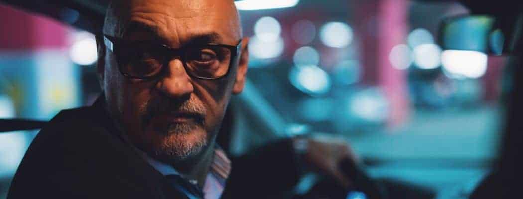 bald man driving at night with glasses