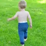 Baby wearing navy and bright blue striped upcycled sweater pants walks on green grass.