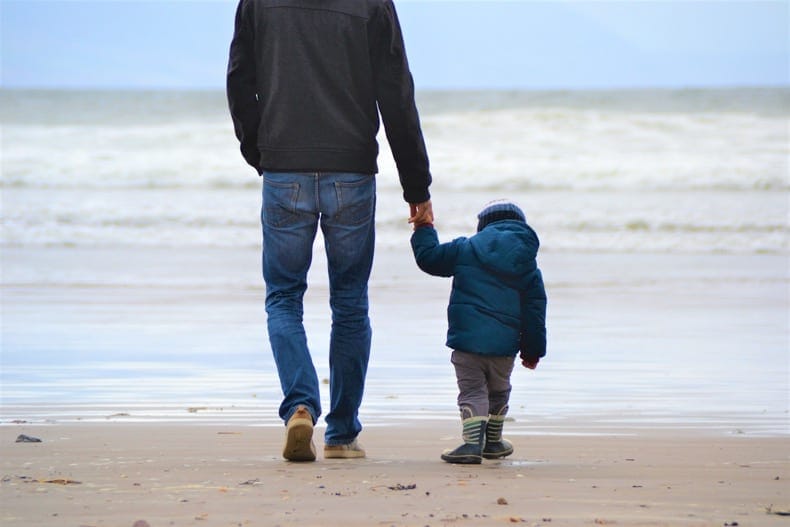 little boy holding dad's hand walking on beach