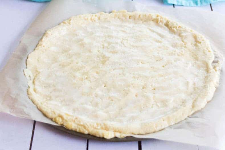 The pizza dough rolled out and shaped on a parchment covered pizza pan.