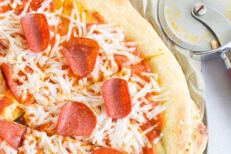 close-up shot of paleo pizza crust with pepperoni and cheese toppings, with a pizza cutter