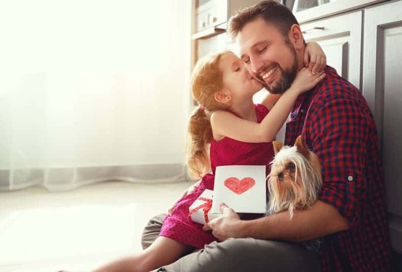 little girl kissing her dad's cheek with a greeting card and gift for dad