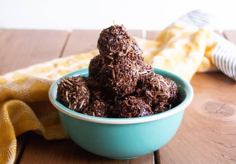 A bowl of chocolate coconut macaroons on a wooden surface with a yellow towel around it