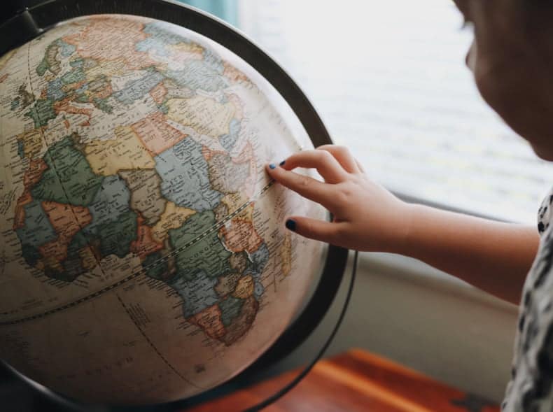 A child is looking at a vintage style globe with their finger pointing to the right of Africa.