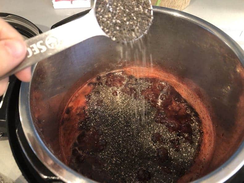 making homemade strawberry jam - pouring chia seeds into the cooked strawberries to thicken