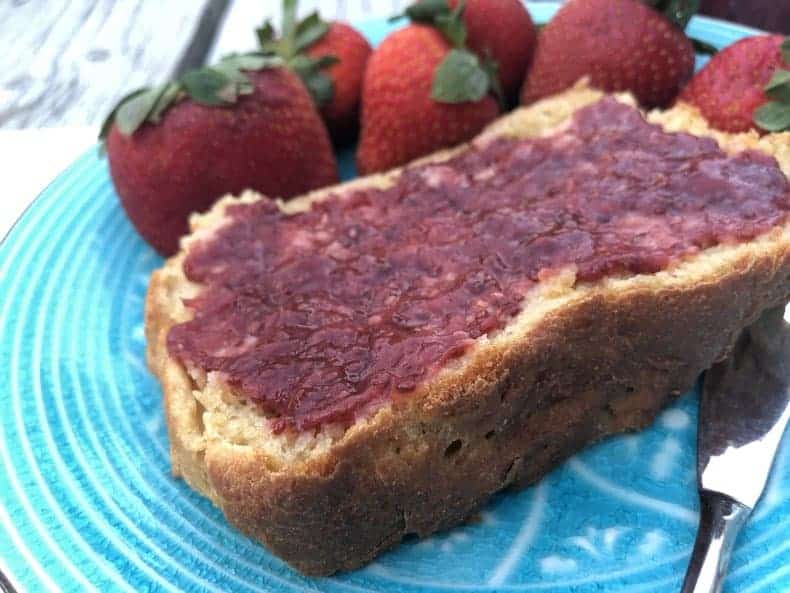 homemade strawberry jam on bread, on a teal plate, with strawberries on the plate