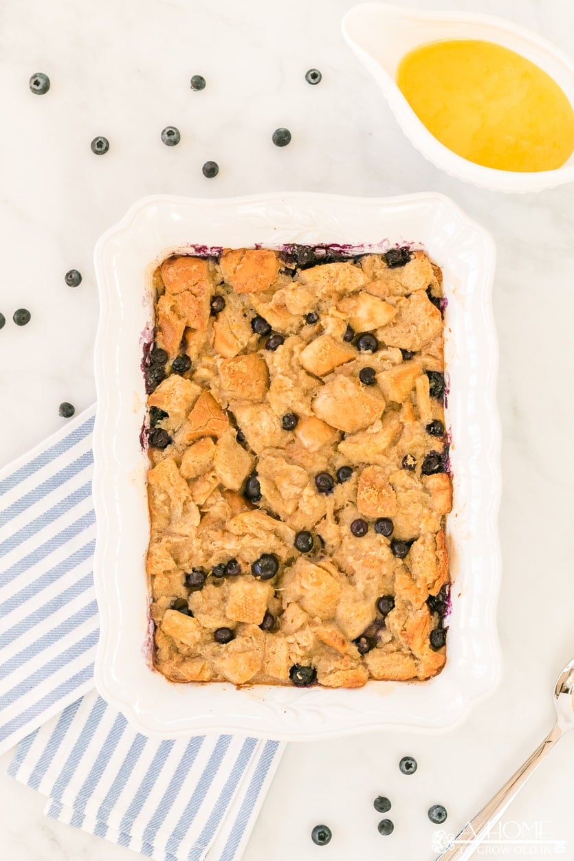 lemon blueberry bread pudding in a baking dish with lemon curd sauce in a pitcher