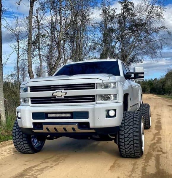 white chevy silverado with shocks and trees background