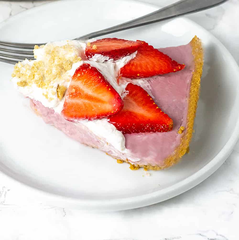 Best vegan strawberry cream pie, pink strawberry pie topped with white vegan coconut whipped cream, sliced strawberries and garnished with sprinkle of crushed golden graham crackers