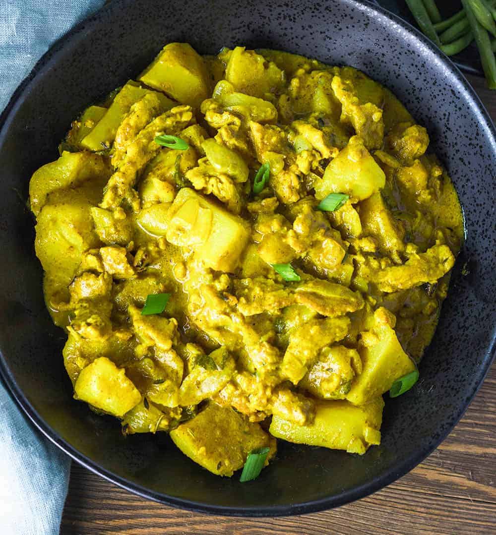vegan curry chicken and potatoes in a black bowl on a wooden background