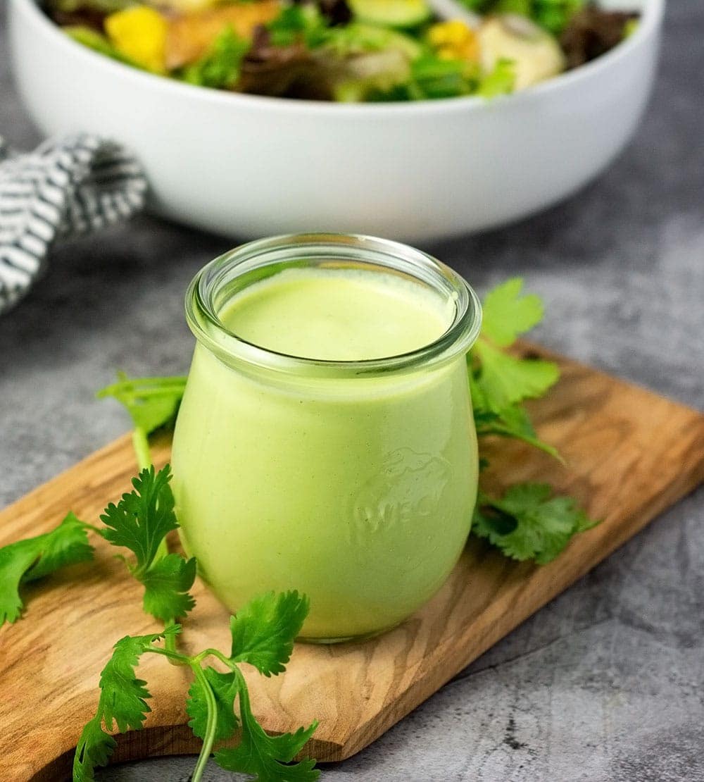 vegan cilantro lime dressing in a glass jar, a blend of cilantro, lime garlic, salt on a wooden cutting board