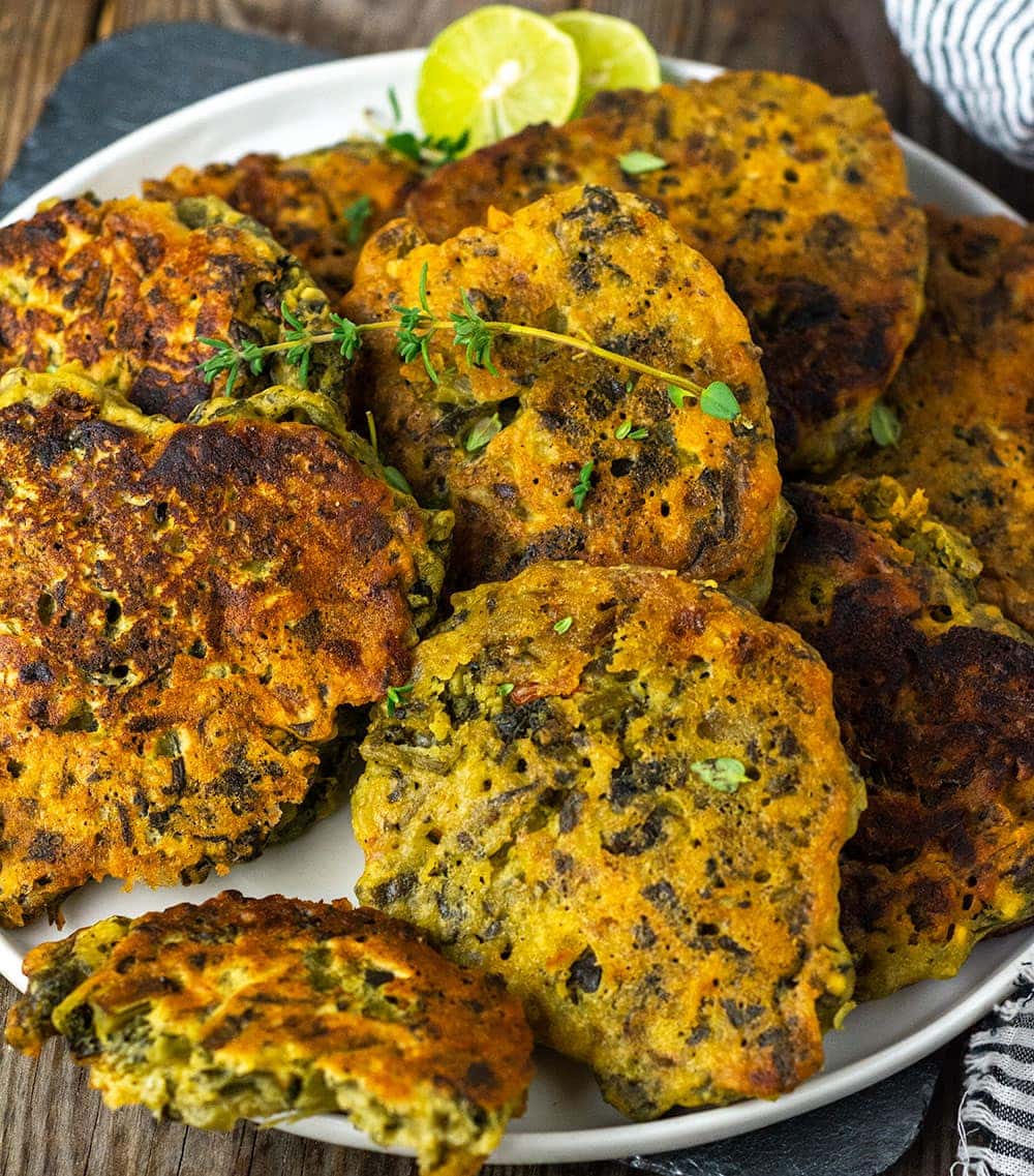 jamaican callaloo fritters recipe with a white plate of callaloo fritters with avocado half in the background and a bowl of ackee with black and white striped napkin