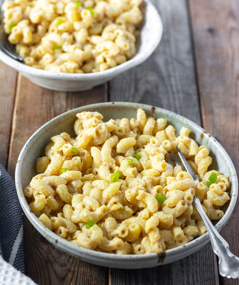 Vegan nut-free mac and cheese in two bowls on a wooden board