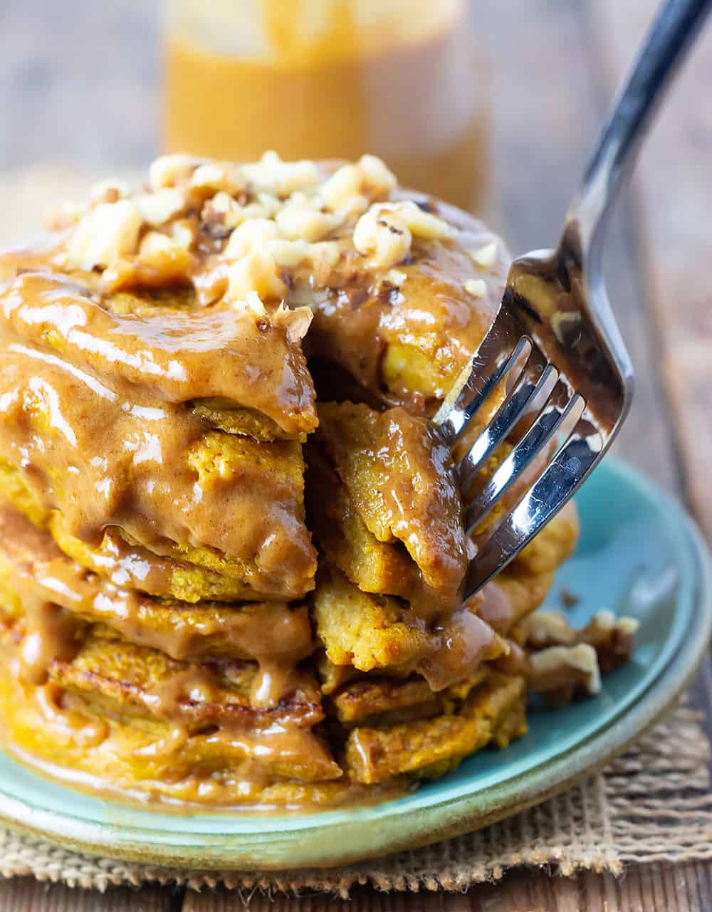 a stack of pumpkin pancakes with sauce drizzling down, and a cut out chunk being removed with a fork