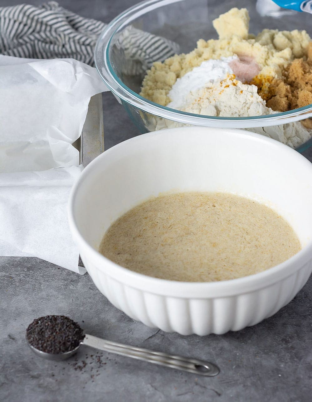 Ingredients for lemon poppy seed bread, bowl with liquid ingredients, silver bowl with dry ingredients, poppy seed in a tablespoon
