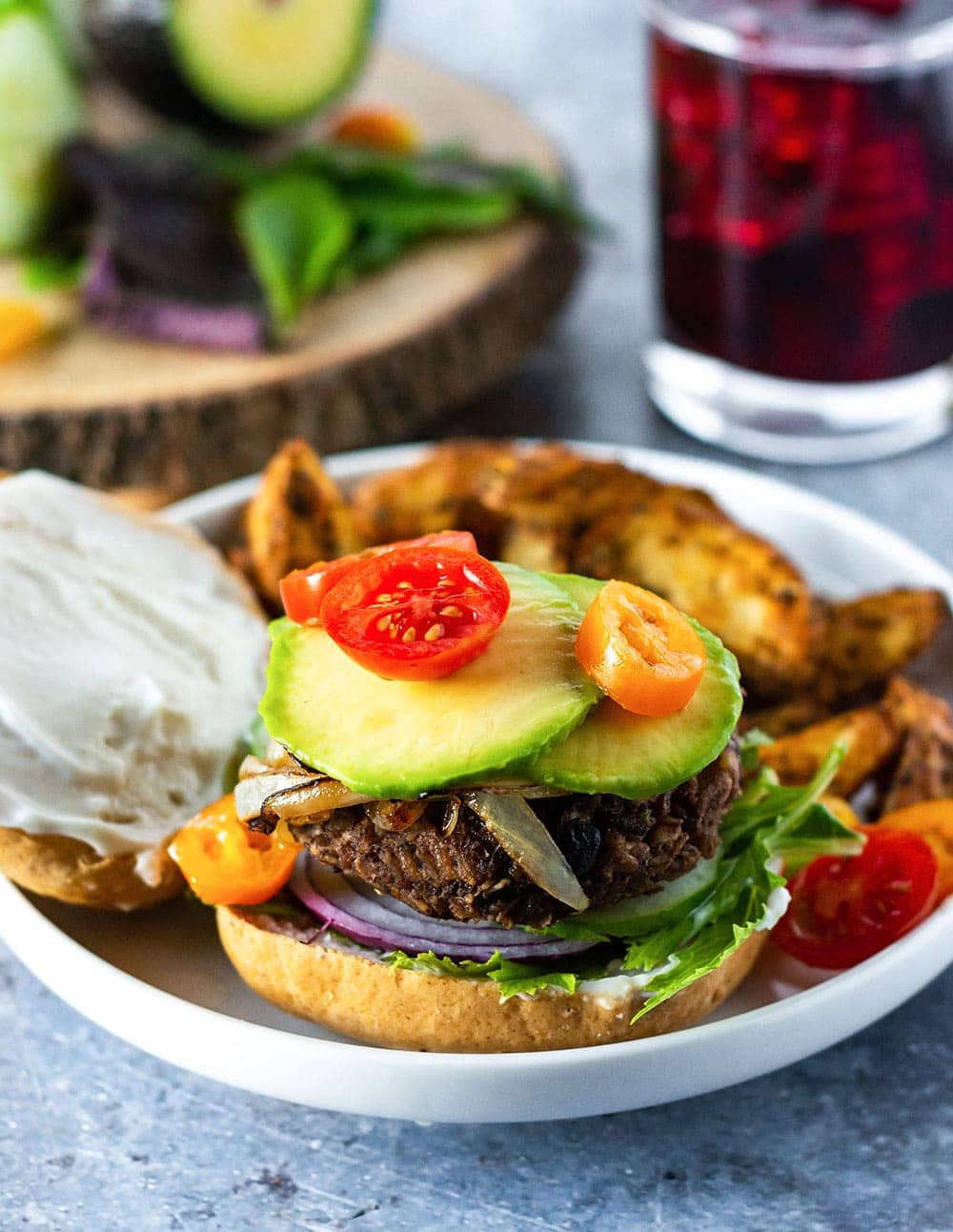 vegan black bean burger on gluten-free vegan bun, with mayo, red onion, caramelized onion, avocado, tomatoes
