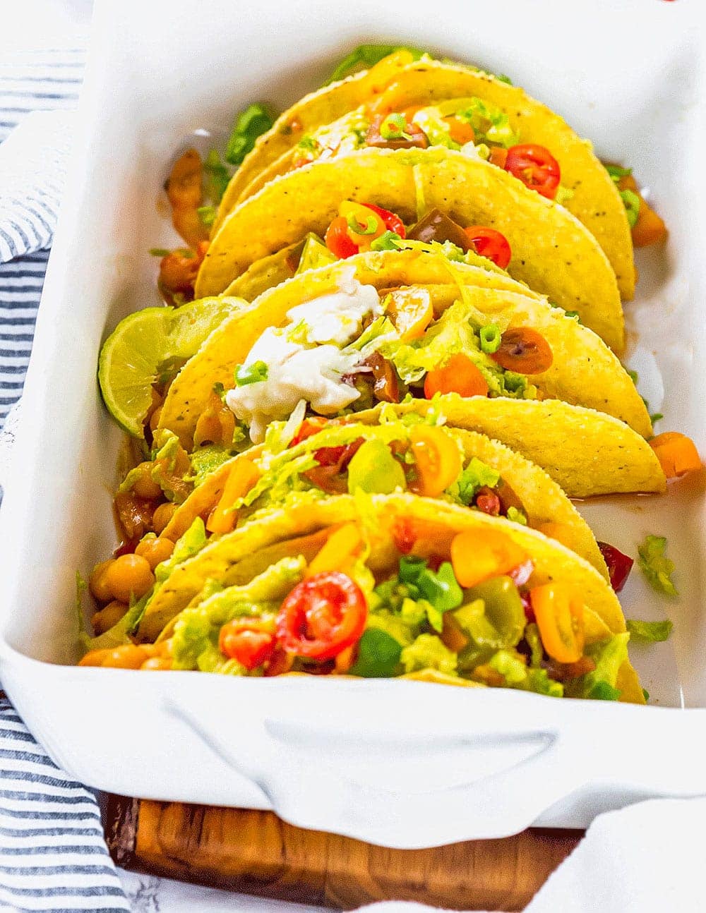 Easy Chickpea Tacos with chickpea stew topped with guacamole, tomatoes, sour cream lettuce in a white casserole dish