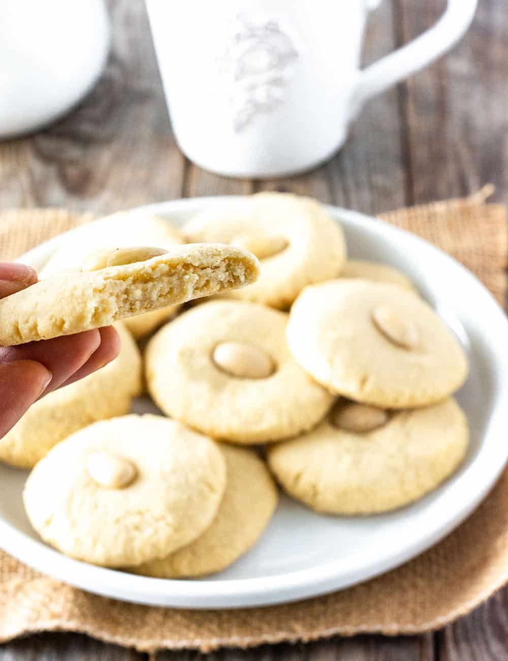 Chinese almond cookies on a white plate with my hand holding a half a cookie