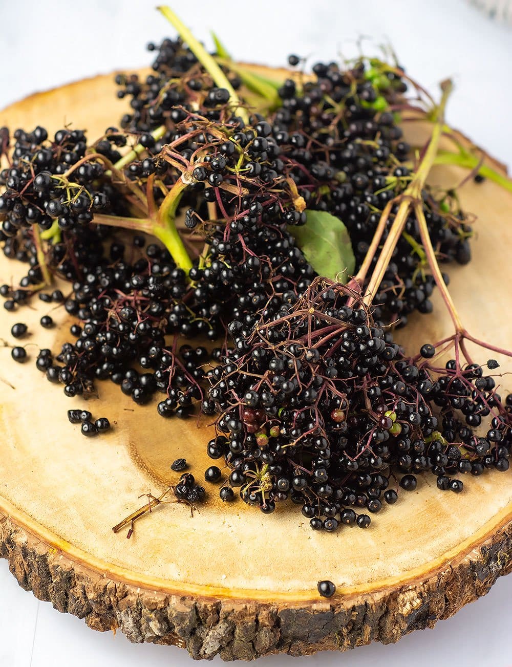 Elderberries for making elderberry syrup on a wooden cutting board with stems and leaves