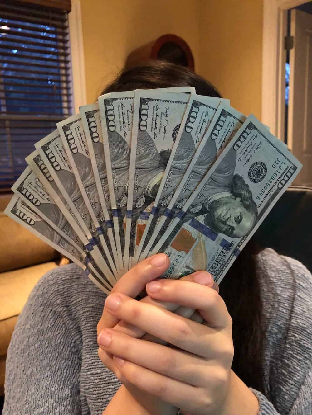 girl fanning pile of money in front of face