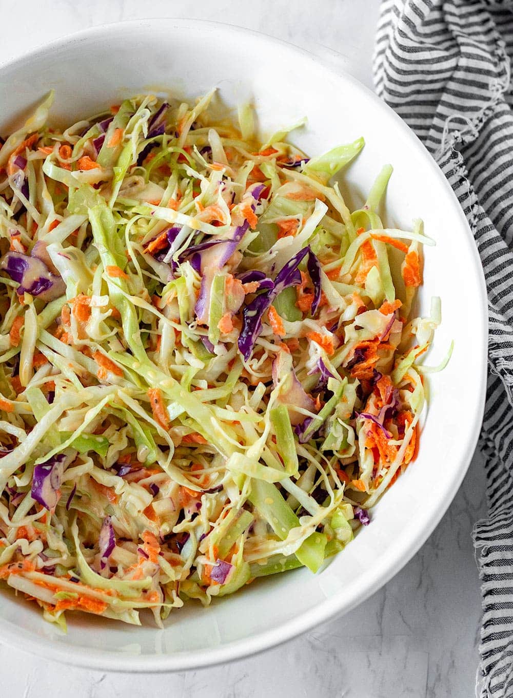 vegan coleslaw recipe with green cabbage, red cabbage, carrots shredded with a creamy vegan coleslaw dressing in a large white bowl
