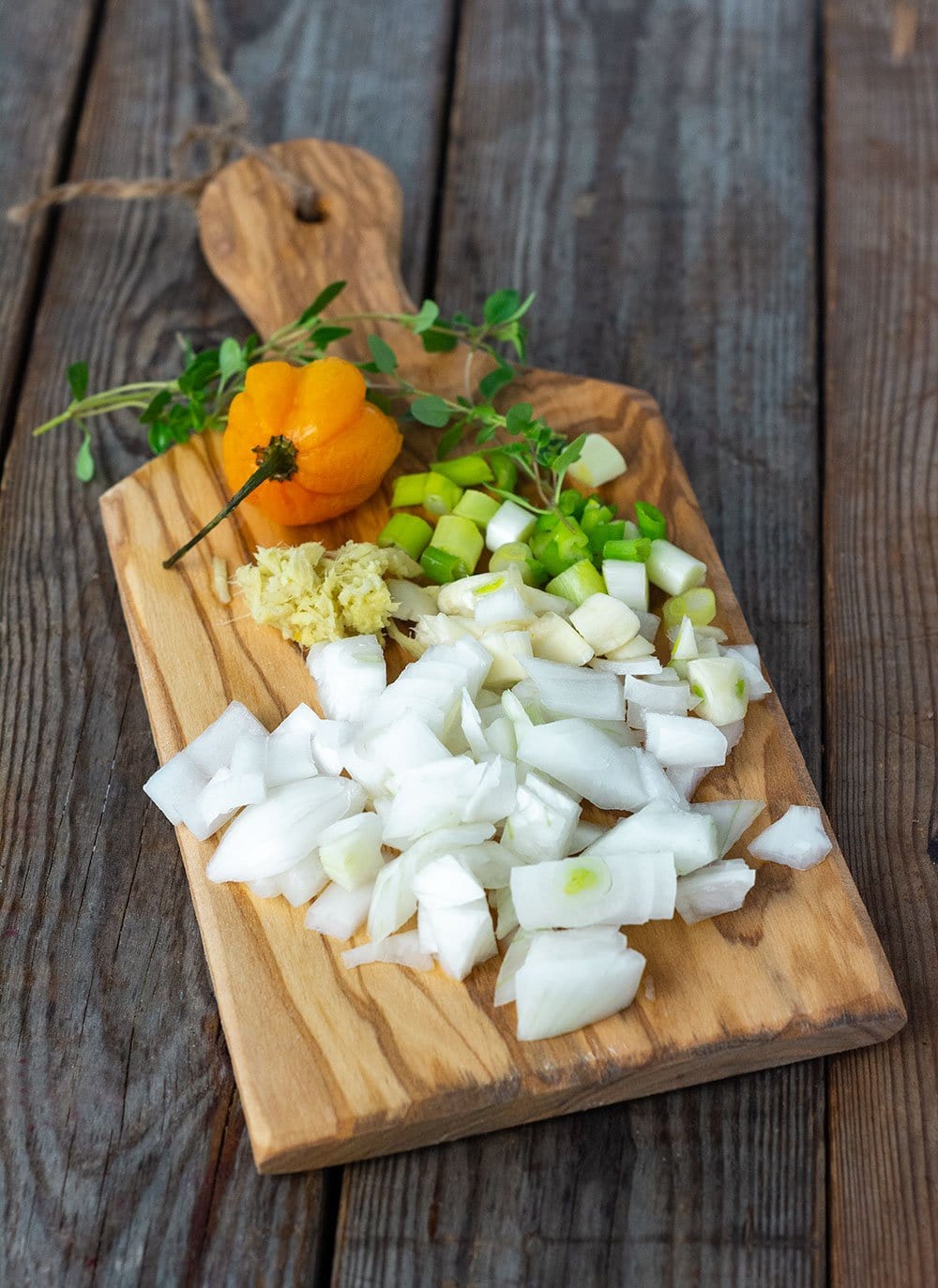 Jamaican pumpkin curry ingredients on a cutting board, chopped onion, garlic, green onion, thyme, scotch bonnet pepper