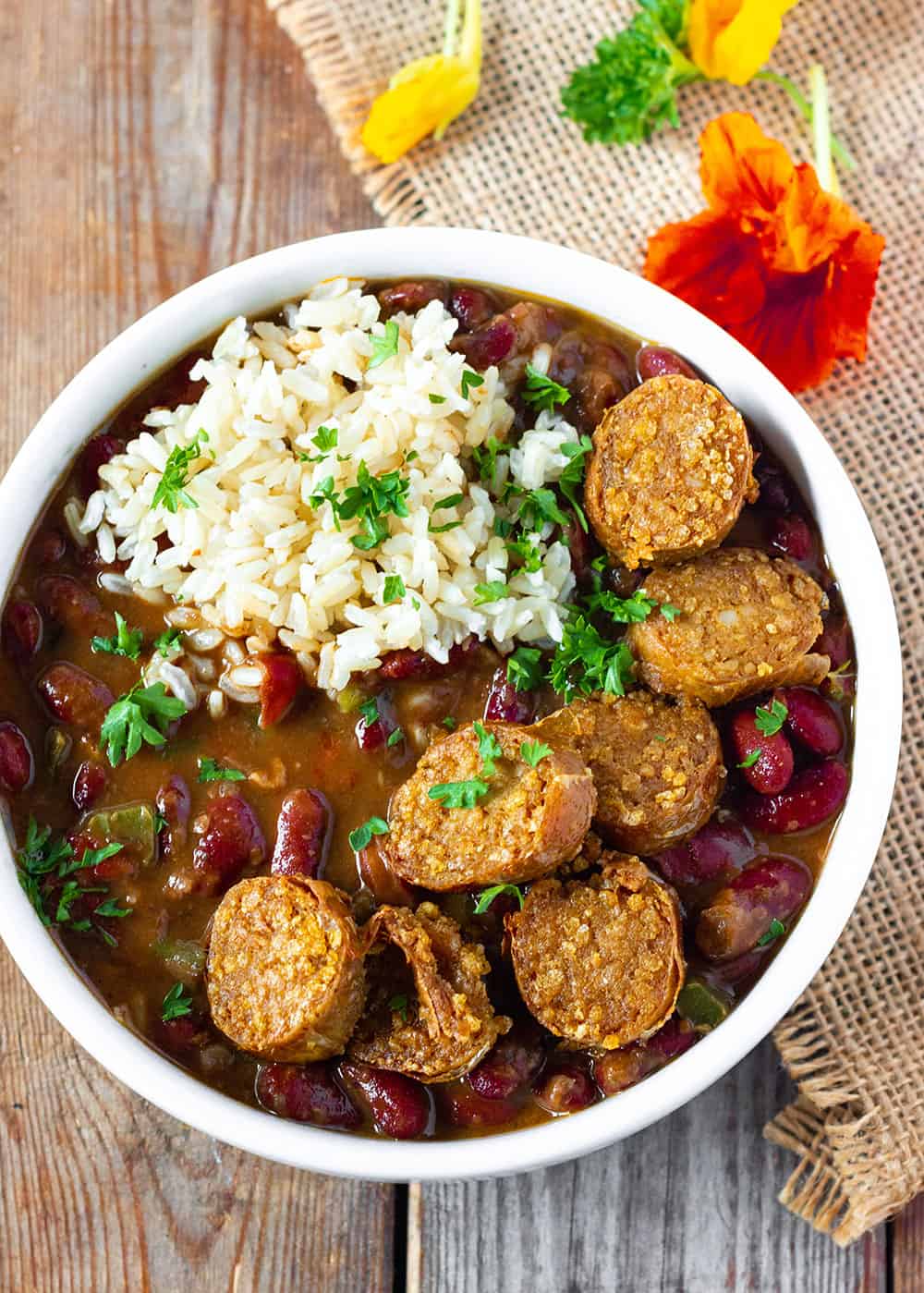 rice smothered with red beans with slices of vegan sausage in a white bowl