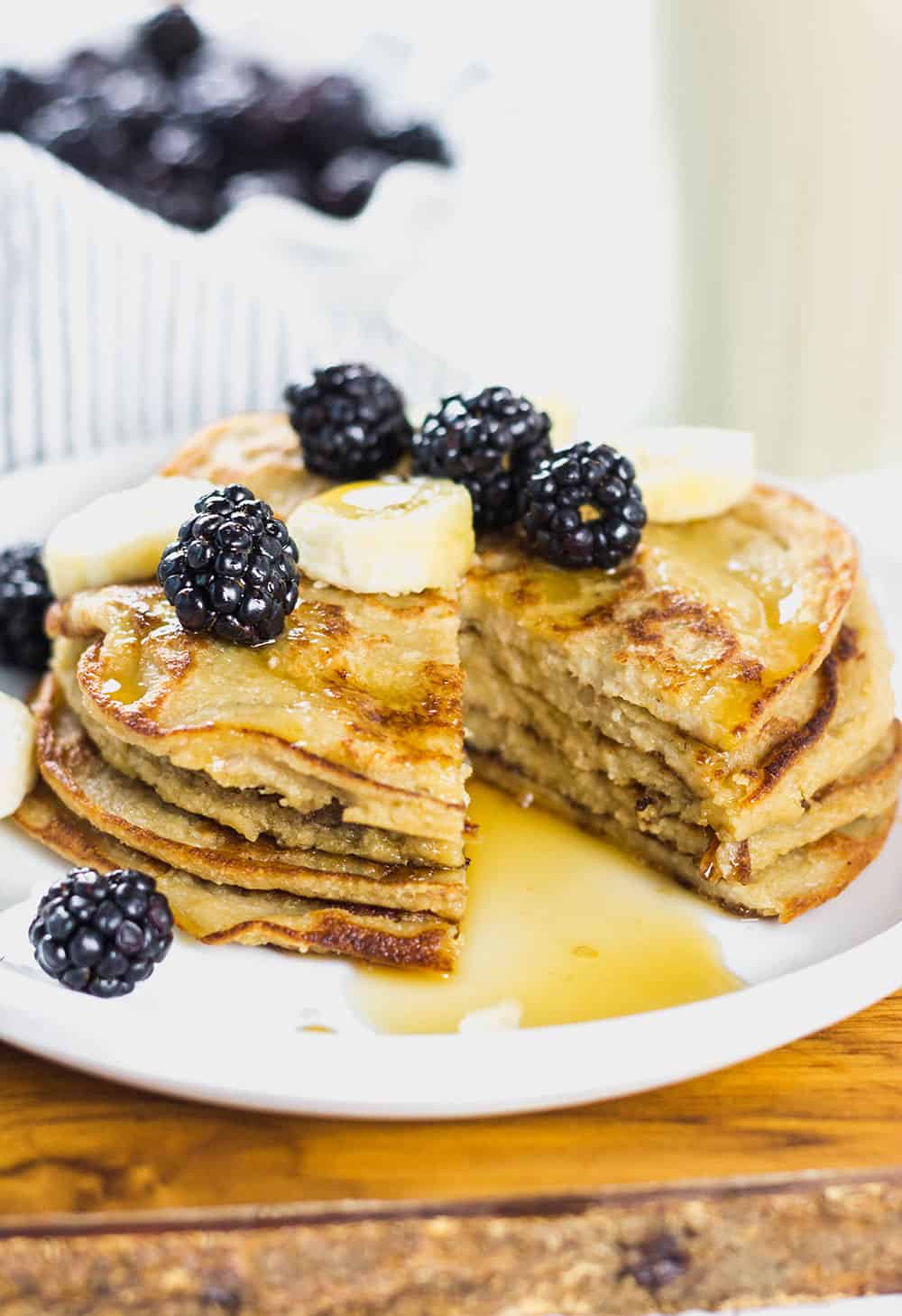 stack of pancakes with bananas, blueberries, and syrup on a white plate with a chunk cut out