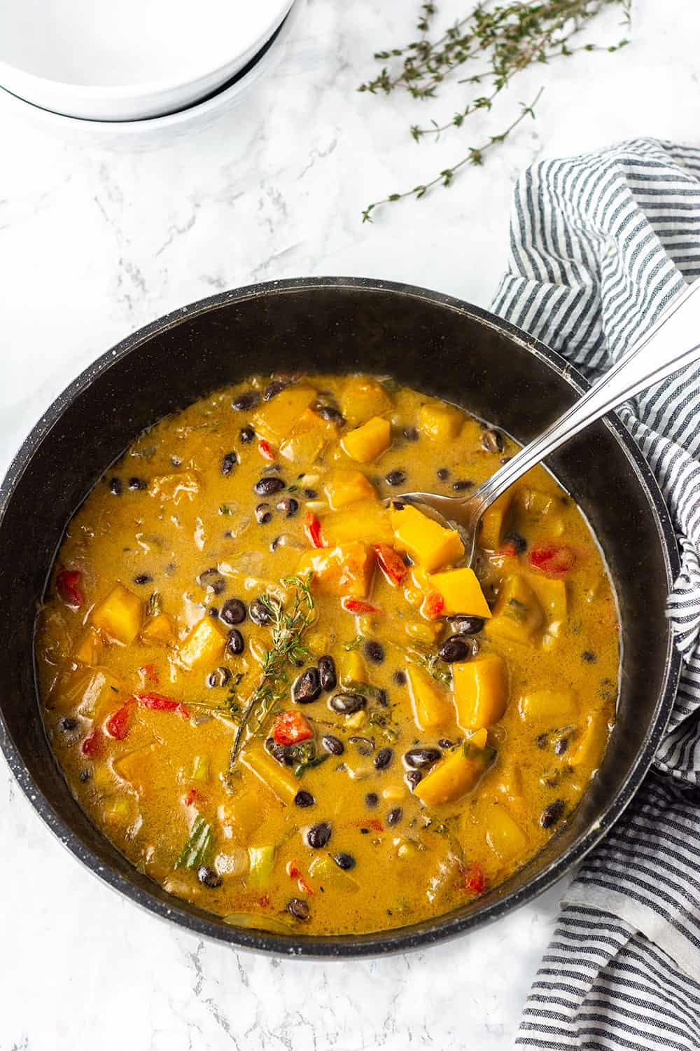 Best black bean and butternut squash stew overhead with thyme garnish red bell pepper and silver spoon