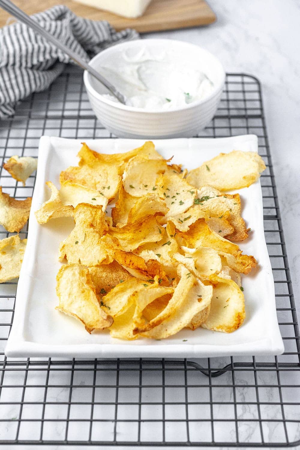 jicama chips on a white rectangular platter with a black and white napkin and a white bowl with yogurt dip